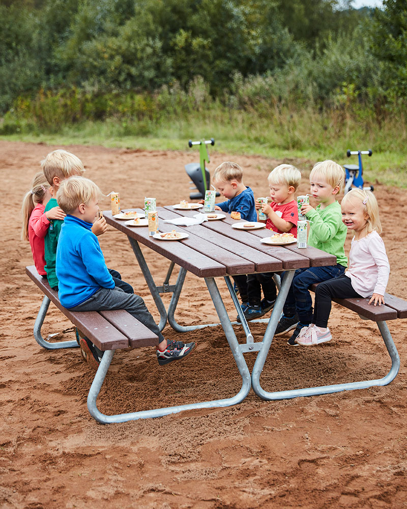 A group of kids on a Linnea picnic table located on a playground.